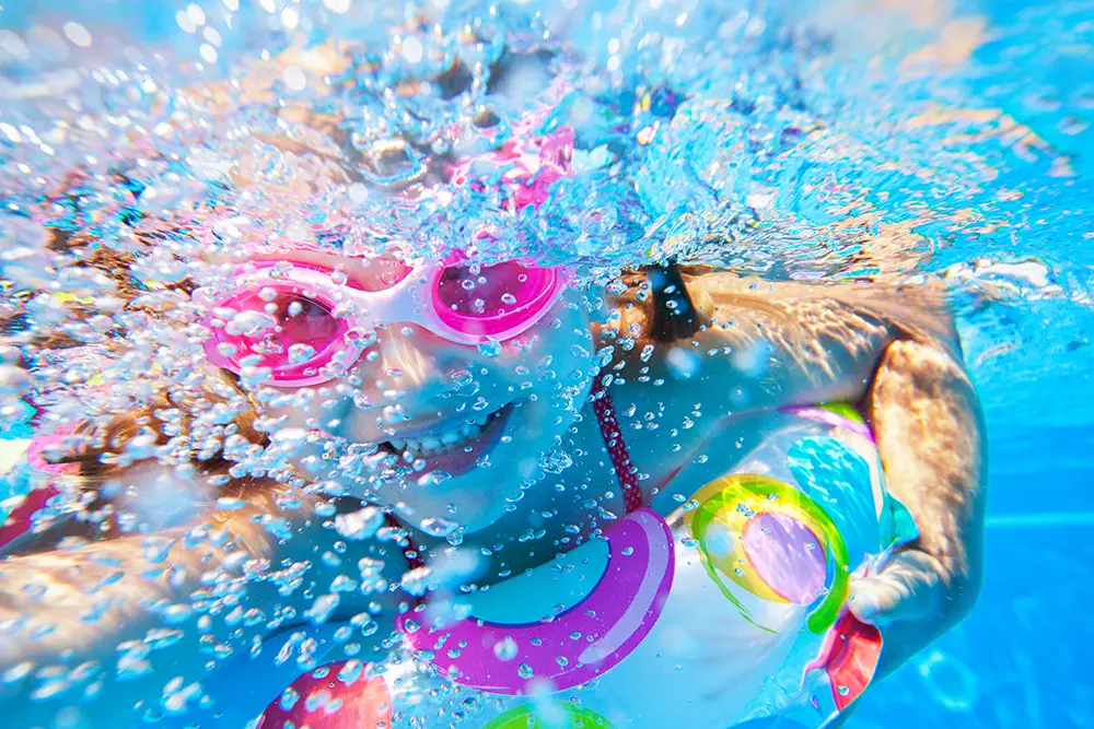 Kind, das den Kopf unter Wasser hält, mit pinker Schwimmbrille